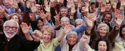 A large multigenerational, multiracial, and multiethnic group of adults standing together, smiling and raising their hands in the air 